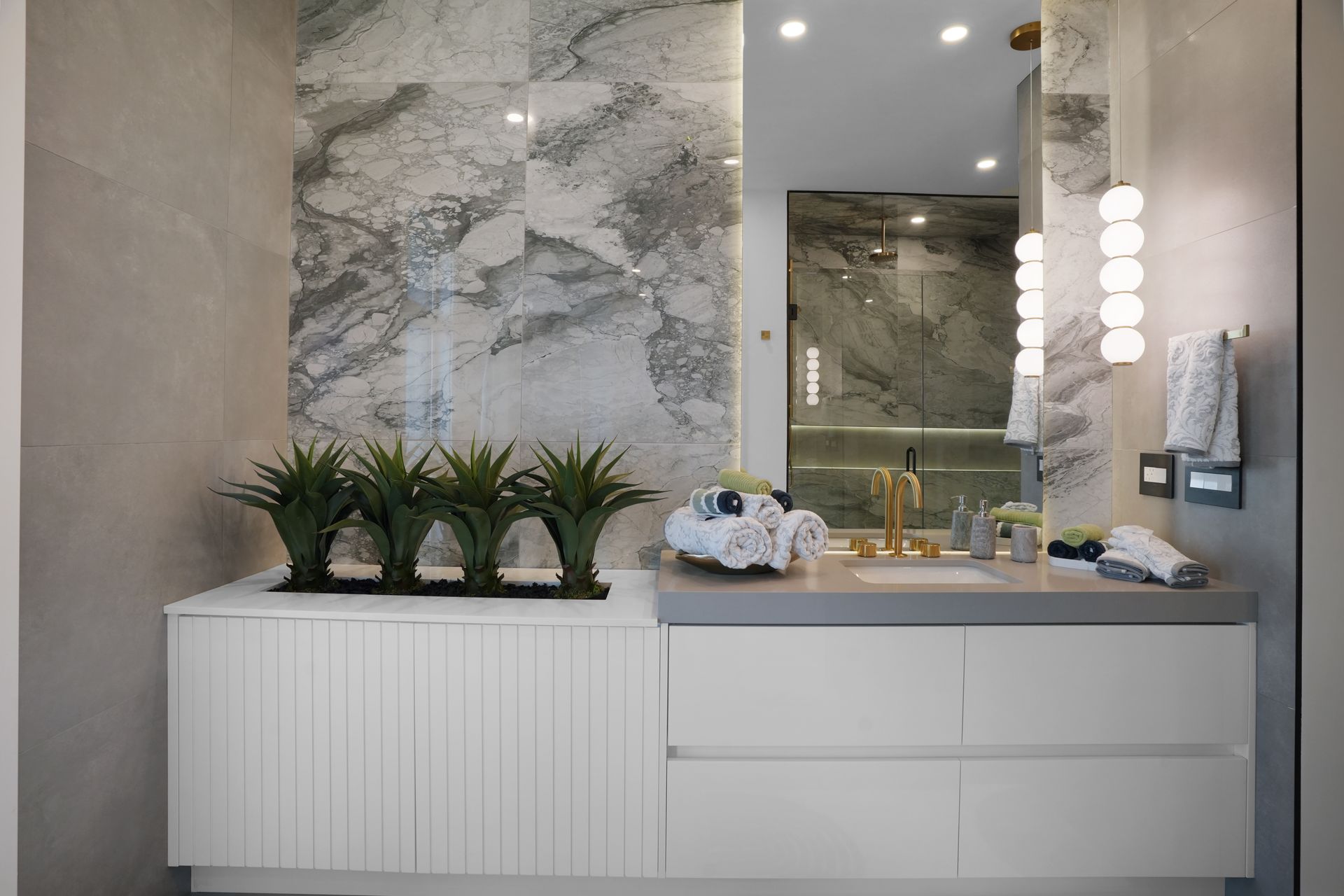 A bathroom with a sink , mirror and plants on the counter.