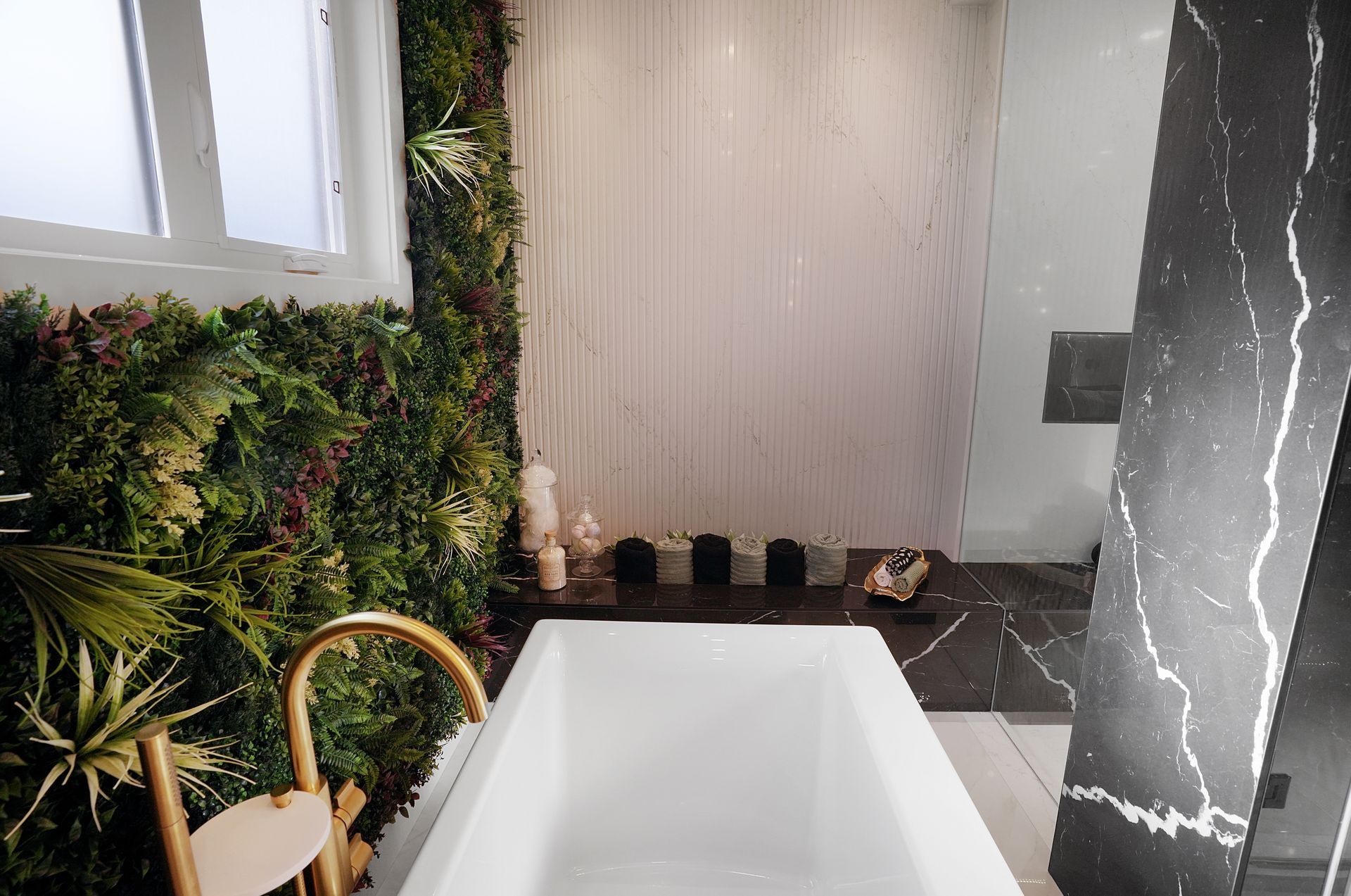 Modern bathroom with a white tub, green wall, and a black marble accent wall.