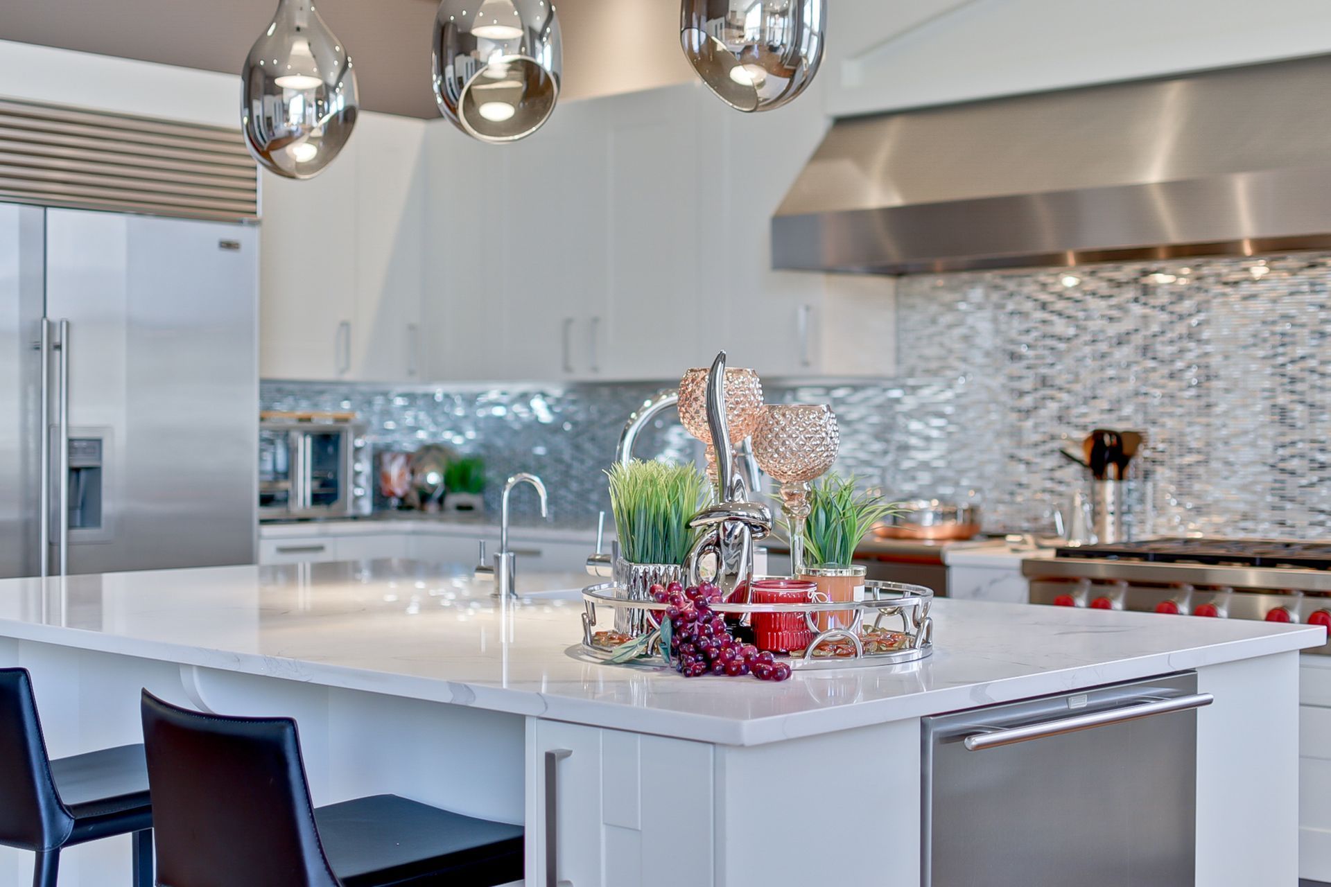 Modern white kitchen with island, stainless steel appliances, pendant lights, and decorative items.