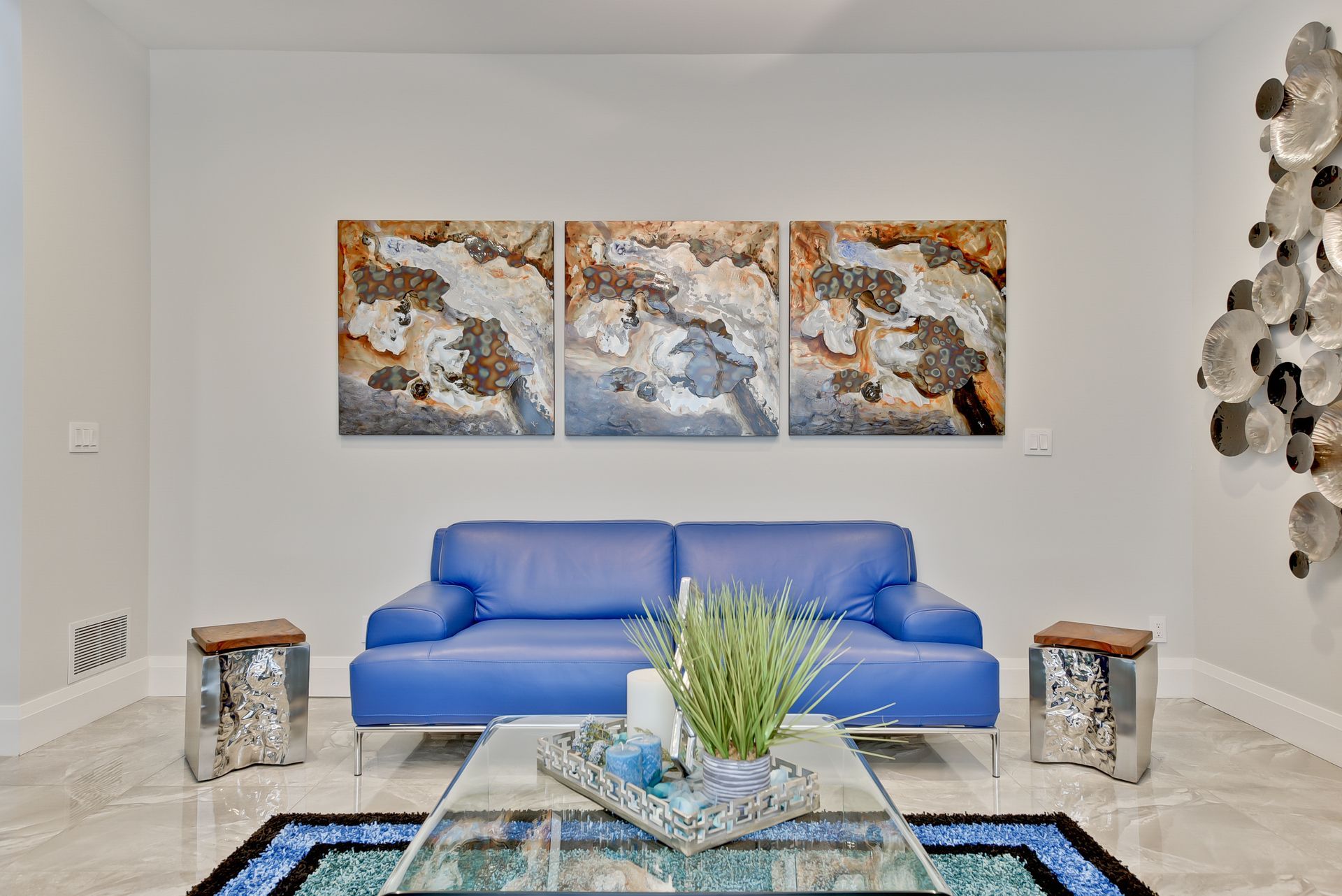 A living room with a blue couch , coffee table , and paintings on the wall.