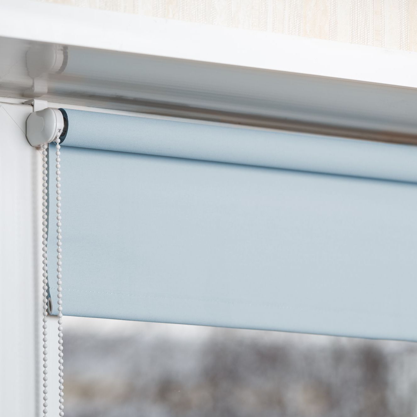 A light blue roller blind is hanging on a window