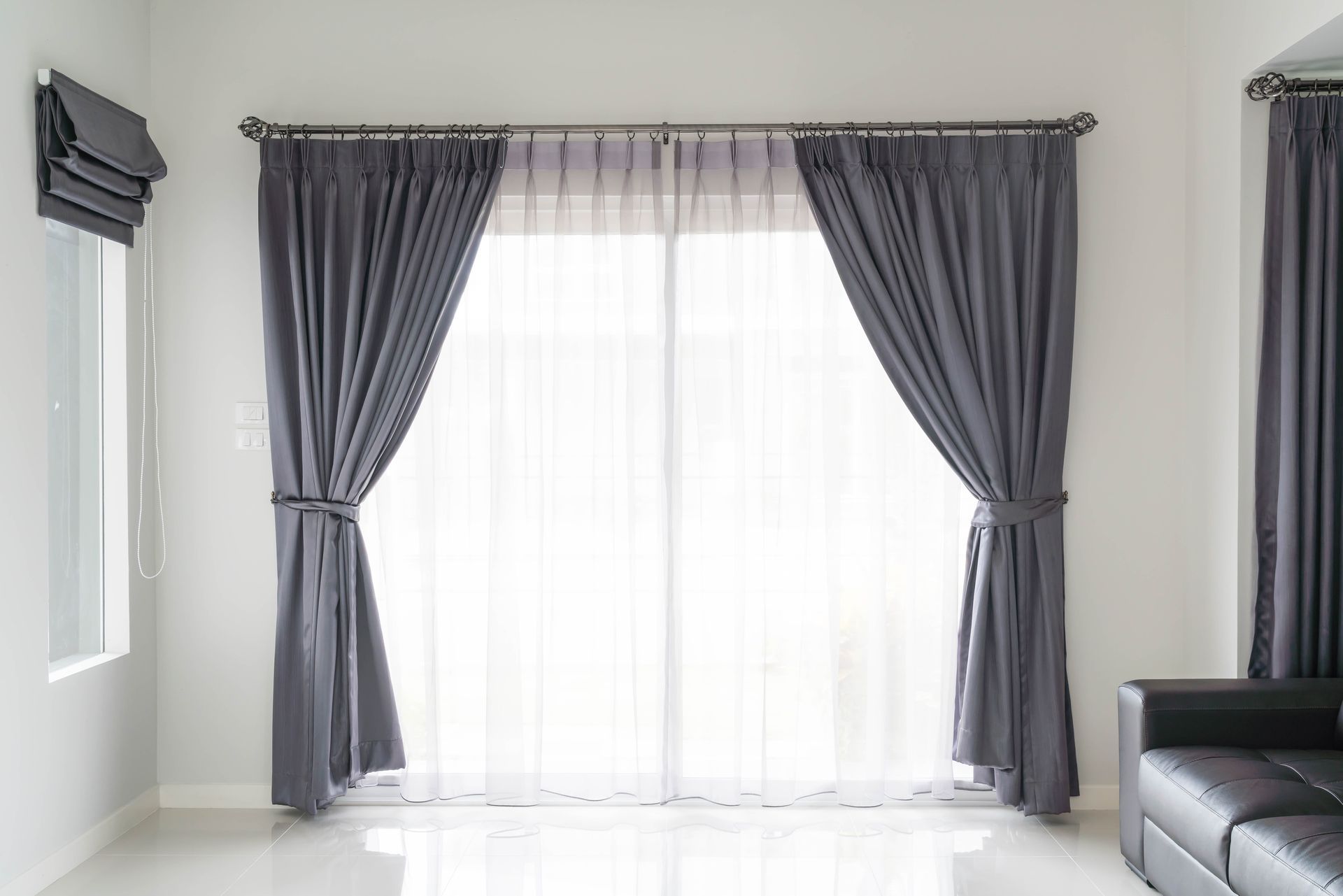 Gray curtains frame a window, tied back to reveal a sheer white curtain. A Roman shade is to the left.