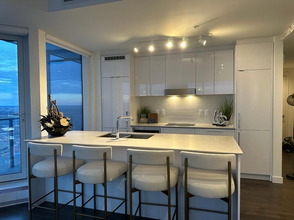 A kitchen with white cabinets and stools and a large island.