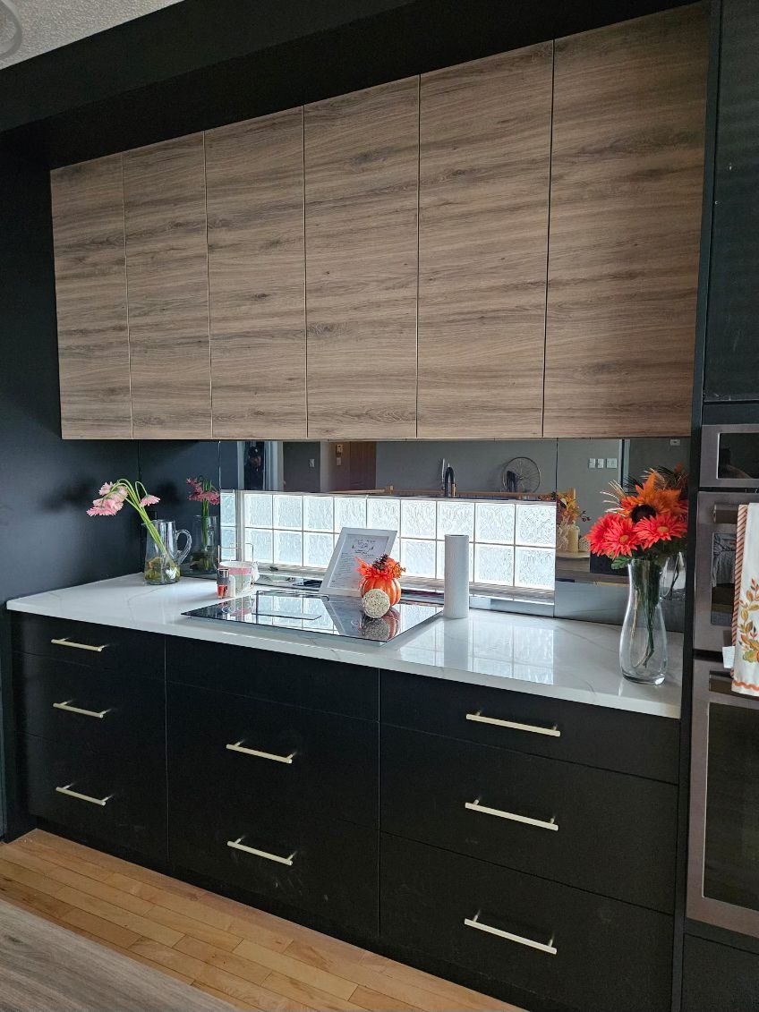 A kitchen with black cabinets , white counter tops , and wooden cabinets.