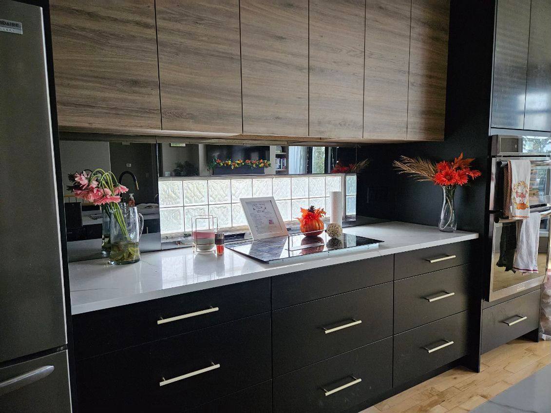 A kitchen with black cabinets , a stove top oven , a refrigerator , and a laptop on the counter.