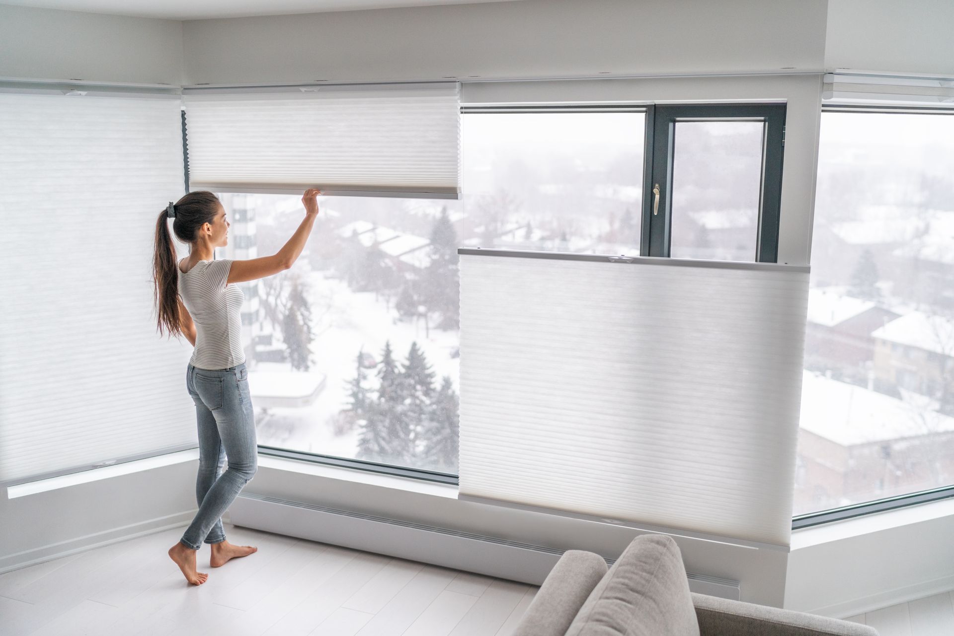 Woman adjusting a white window shade, looking out at a snowy landscape.