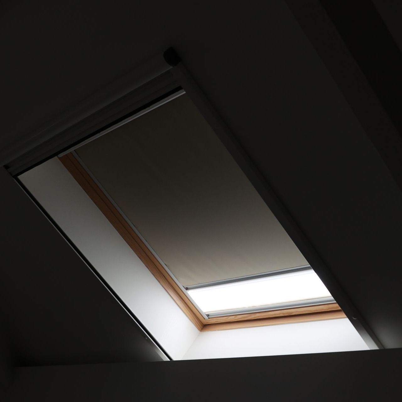 Skylight with a partially closed shade, allowing light to enter.