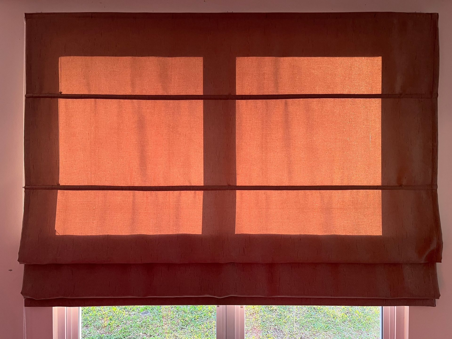 Brown Roman shade over a window, lit by sunlight.