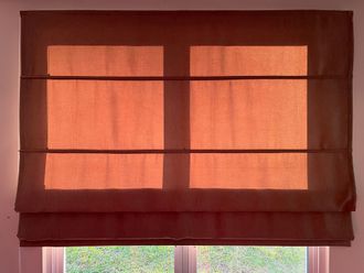 Brown Roman shade over a window, lit by sunlight.
