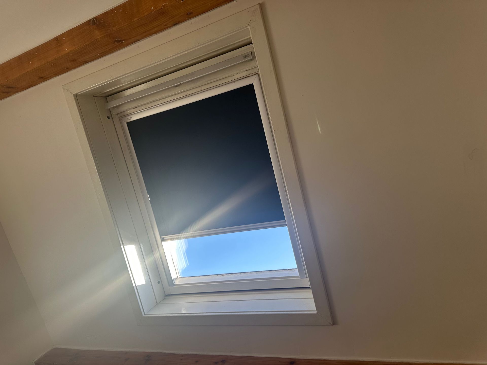 Skylight with a closed dark blue shade in a white-walled room, sunlight streaming in.