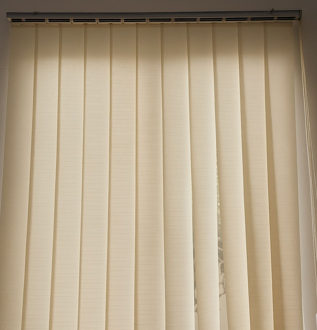 Cream-colored vertical blinds, partially open, hanging in front of a window.