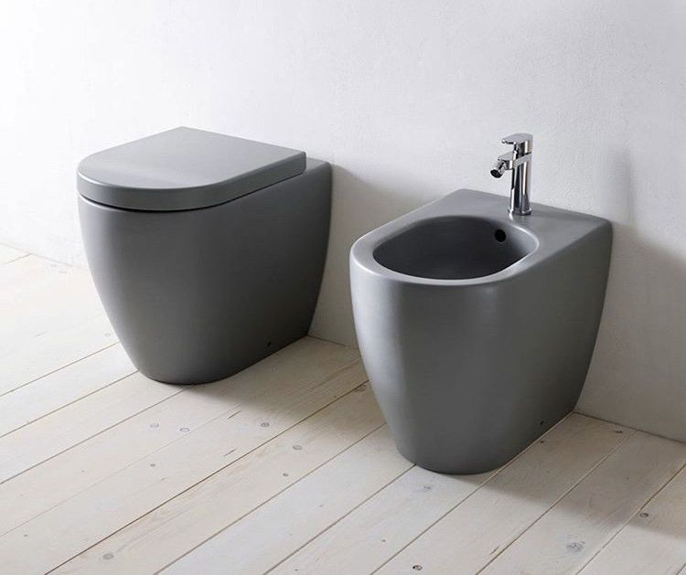 Un water e un bidet sono appoggiati su un pavimento in legno in un bagno.