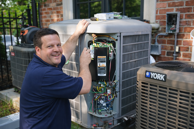 A technician smiles while repairing the electrical control panel of an outdoor residential air conditioning unit.