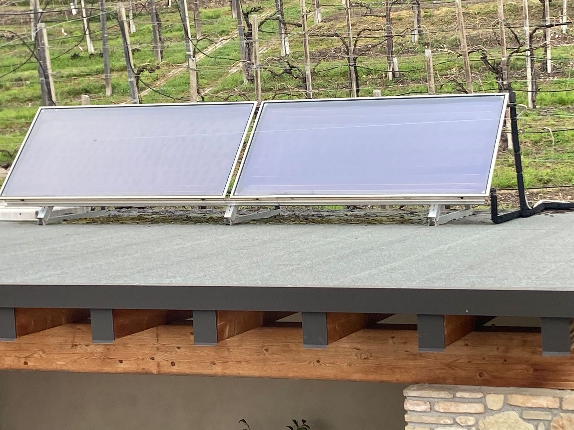 Mano guantata che tocca un pannello solare. Guanto arancione, pannelli disposti su una superficie.