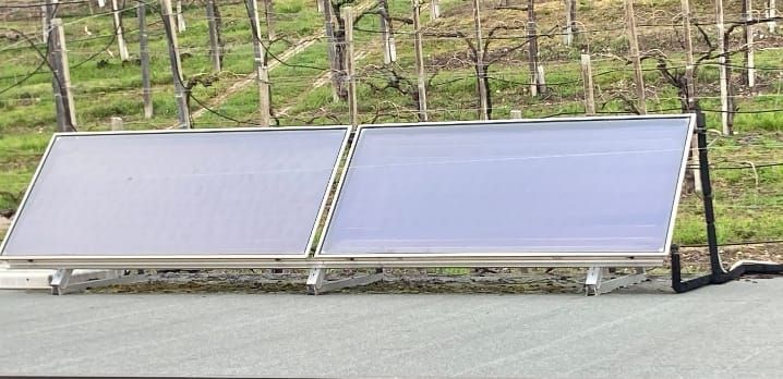 Mano guantata che tocca un pannello solare. Guanto arancione, pannelli disposti su una superficie.