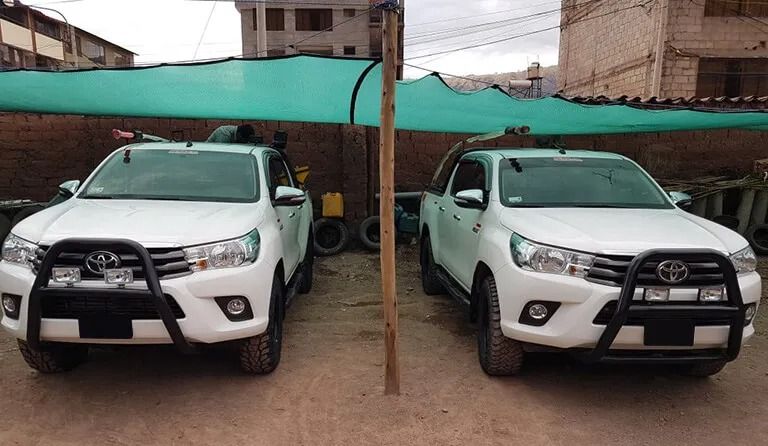 Aparcamiento de coches de alquiler con una camioneta blanca llena de equipaje y varios vehículos 