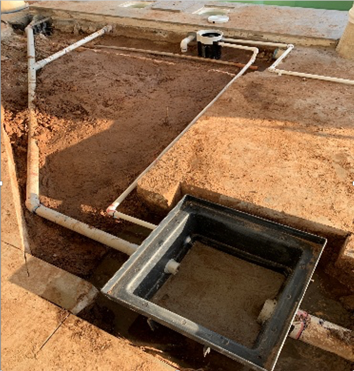 Pool construction: Excavated area with plumbing pipes, a black skimmer box, and sandy ground. — Ausplumb NT in Winnellie, NT