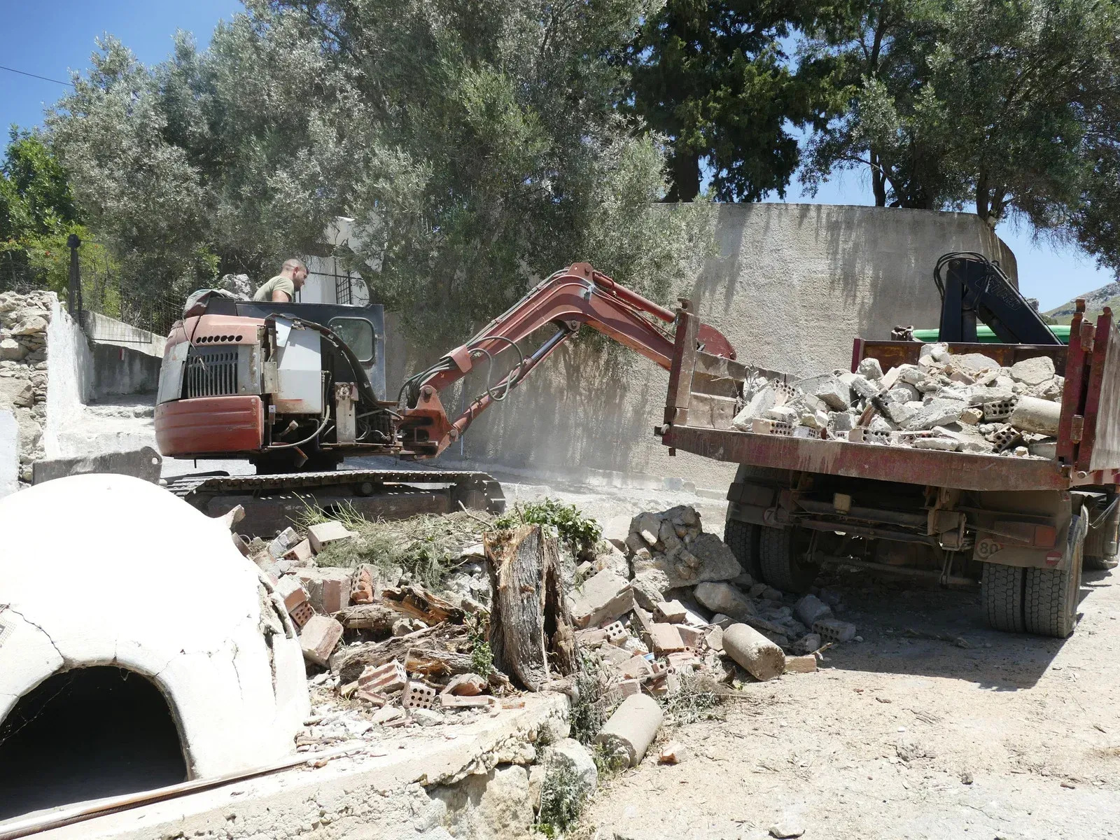Excavator loading debris into a truck at a demolition site; outdoors in daylight.