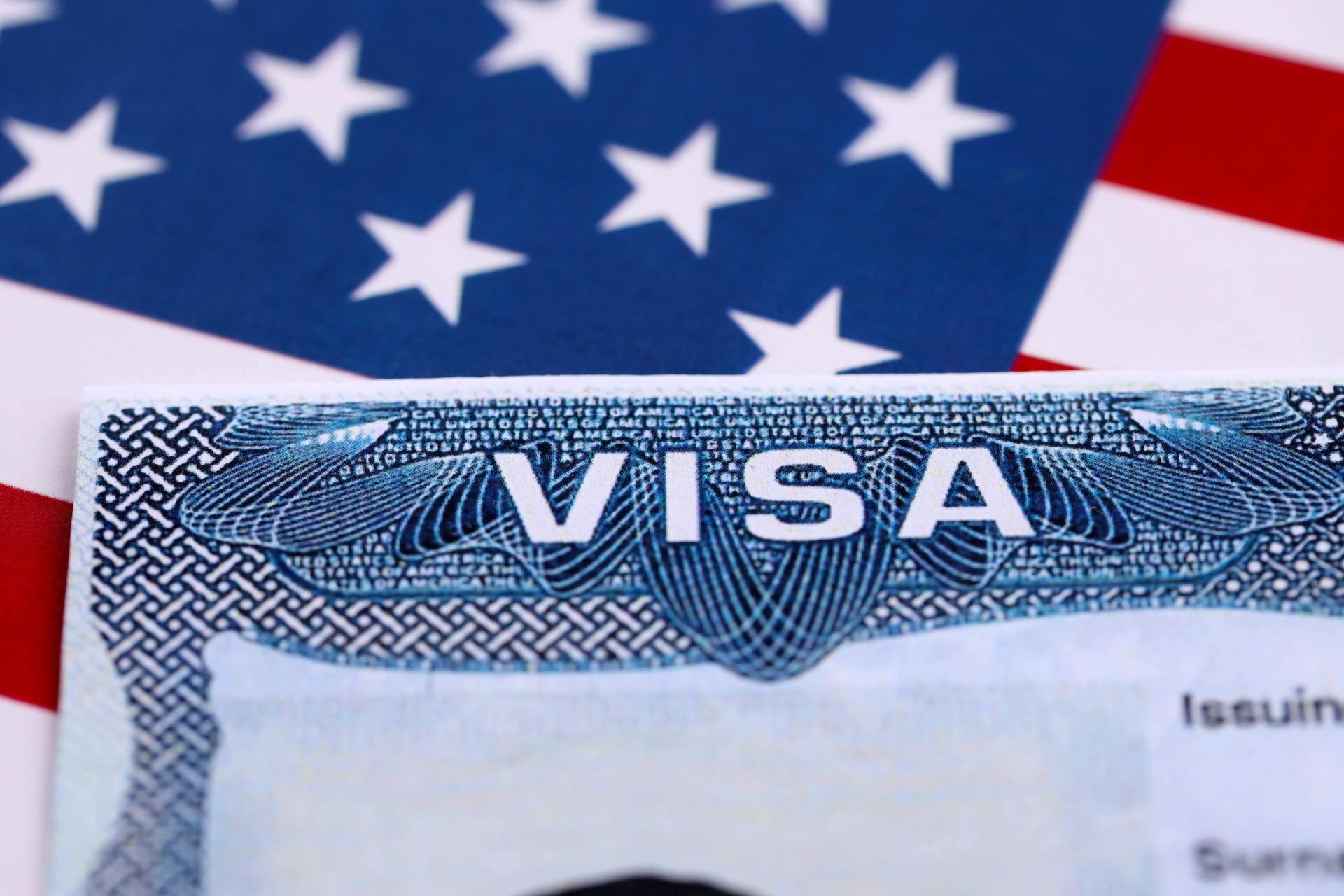 A close-up view of a United States visa document placed over a blurred American flag background.