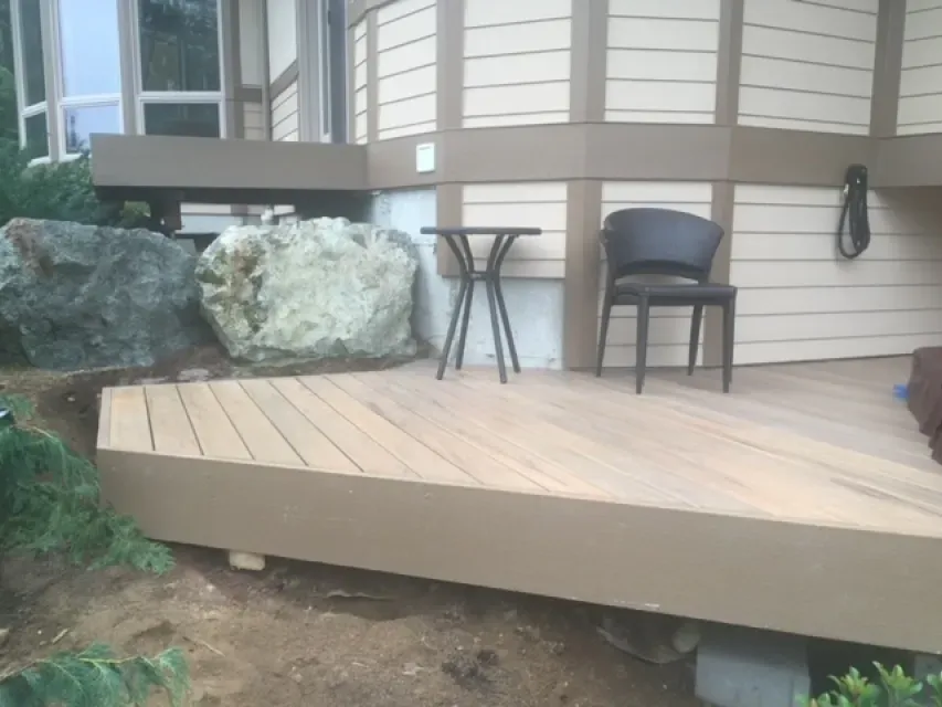A wooden deck with a table and chairs on it in front of a house.