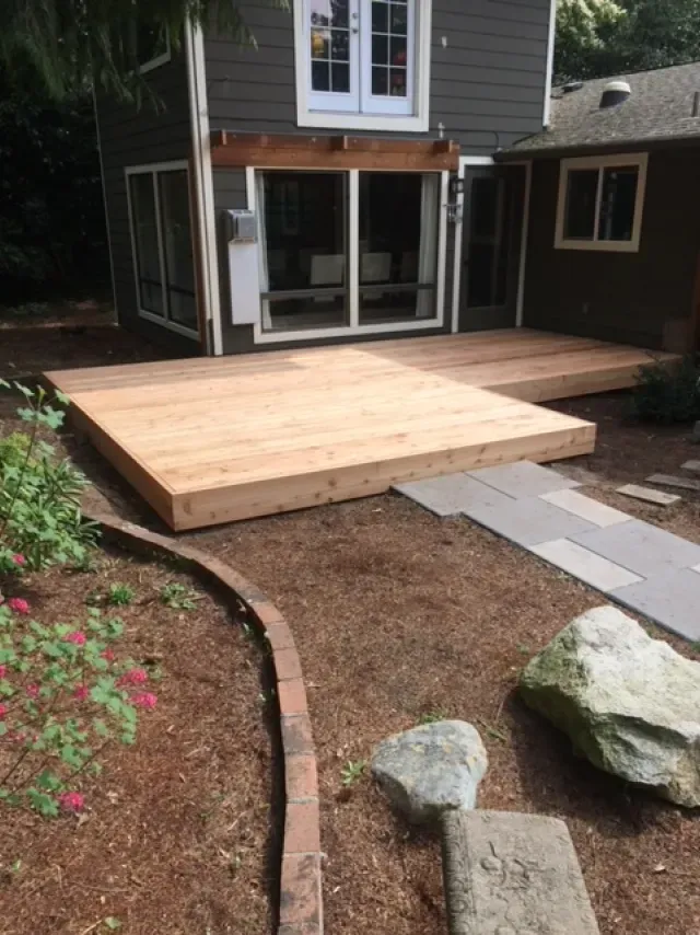 A wooden deck is in the backyard of a house.