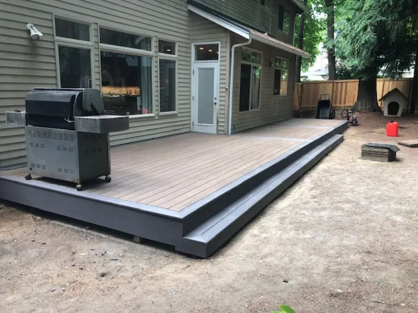 A large deck with a grill on it in front of a house.