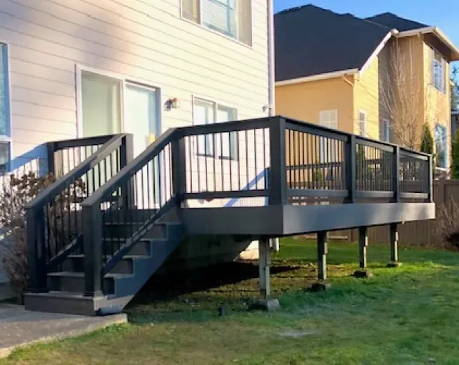 A deck with stairs leading up to it is in the backyard of a house.