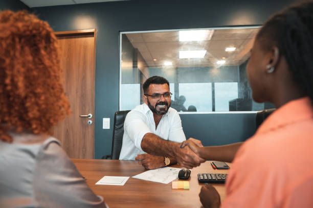 Man in white shirt shakes hands with a woman at a table in an office.