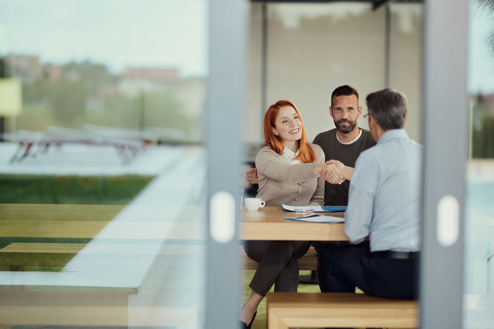 Couple shaking hands with a person at a table, likely a business meeting.