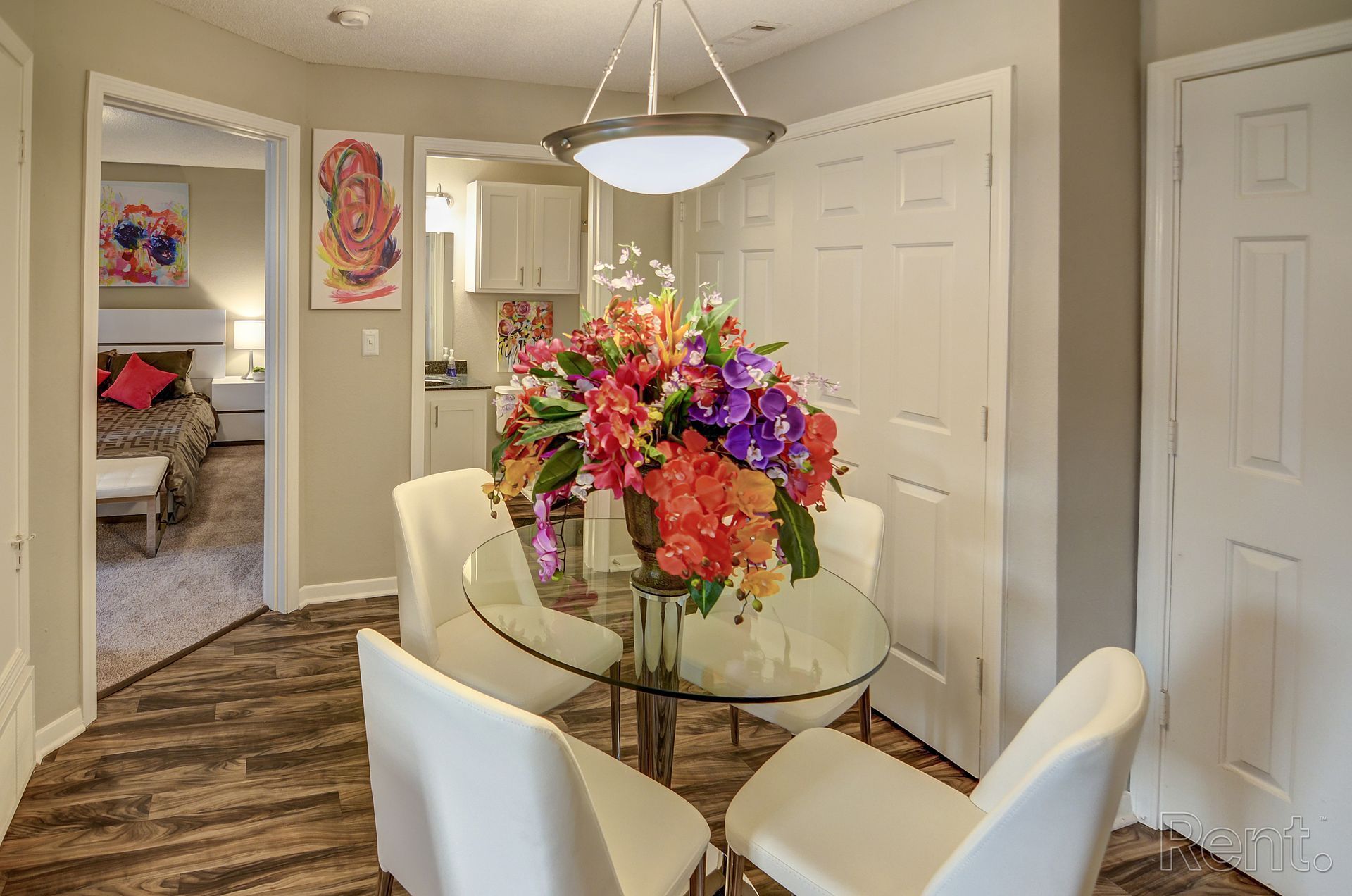A dining room with a glass table and chairs and a vase of flowers.