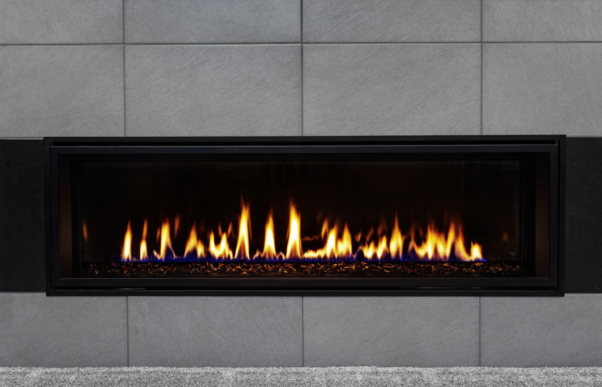 A modern gas fireplace with a black frame and flames, set into a gray tiled wall.