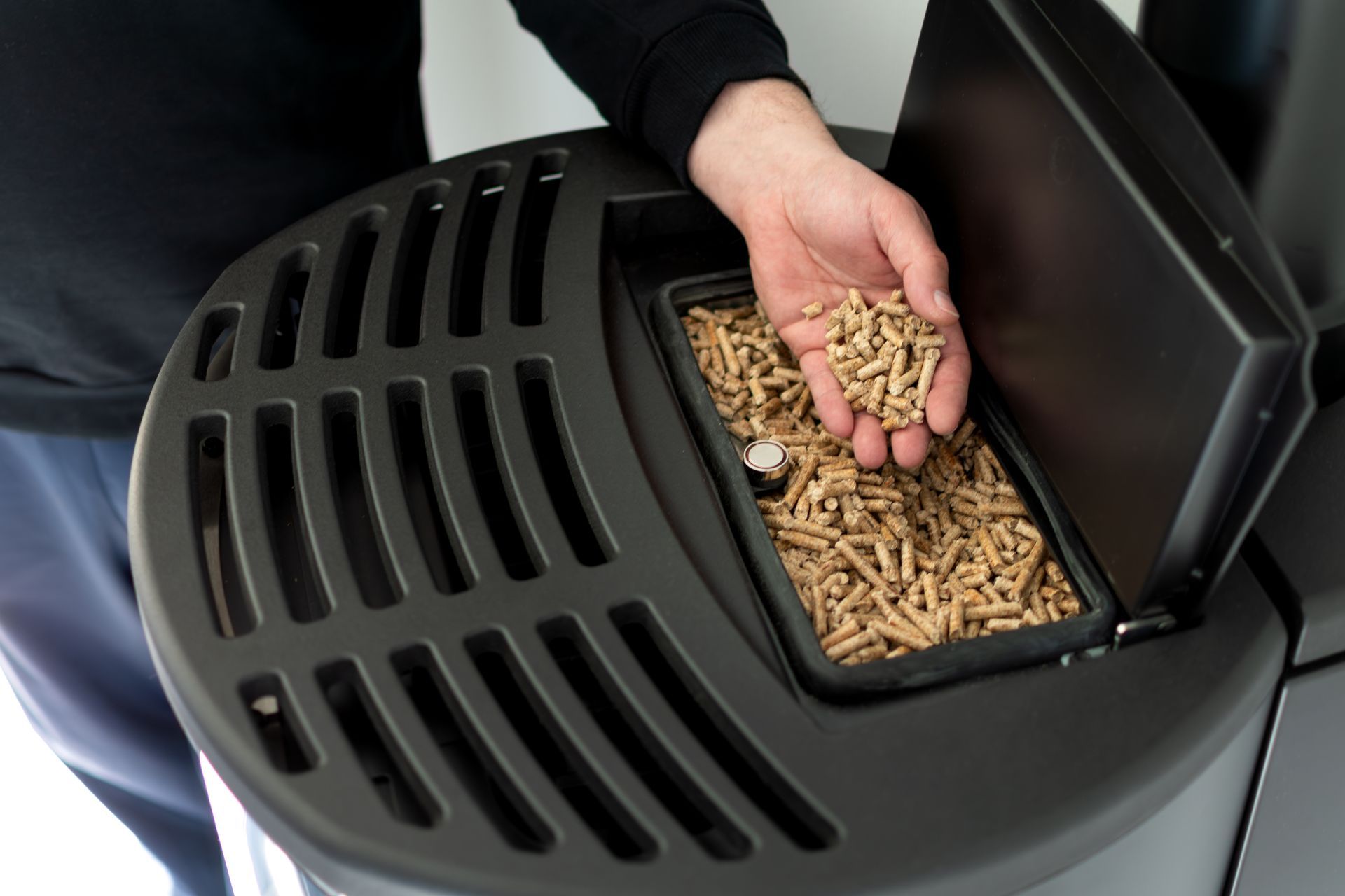 Person filling a pellet stove with wood pellets from an open container.