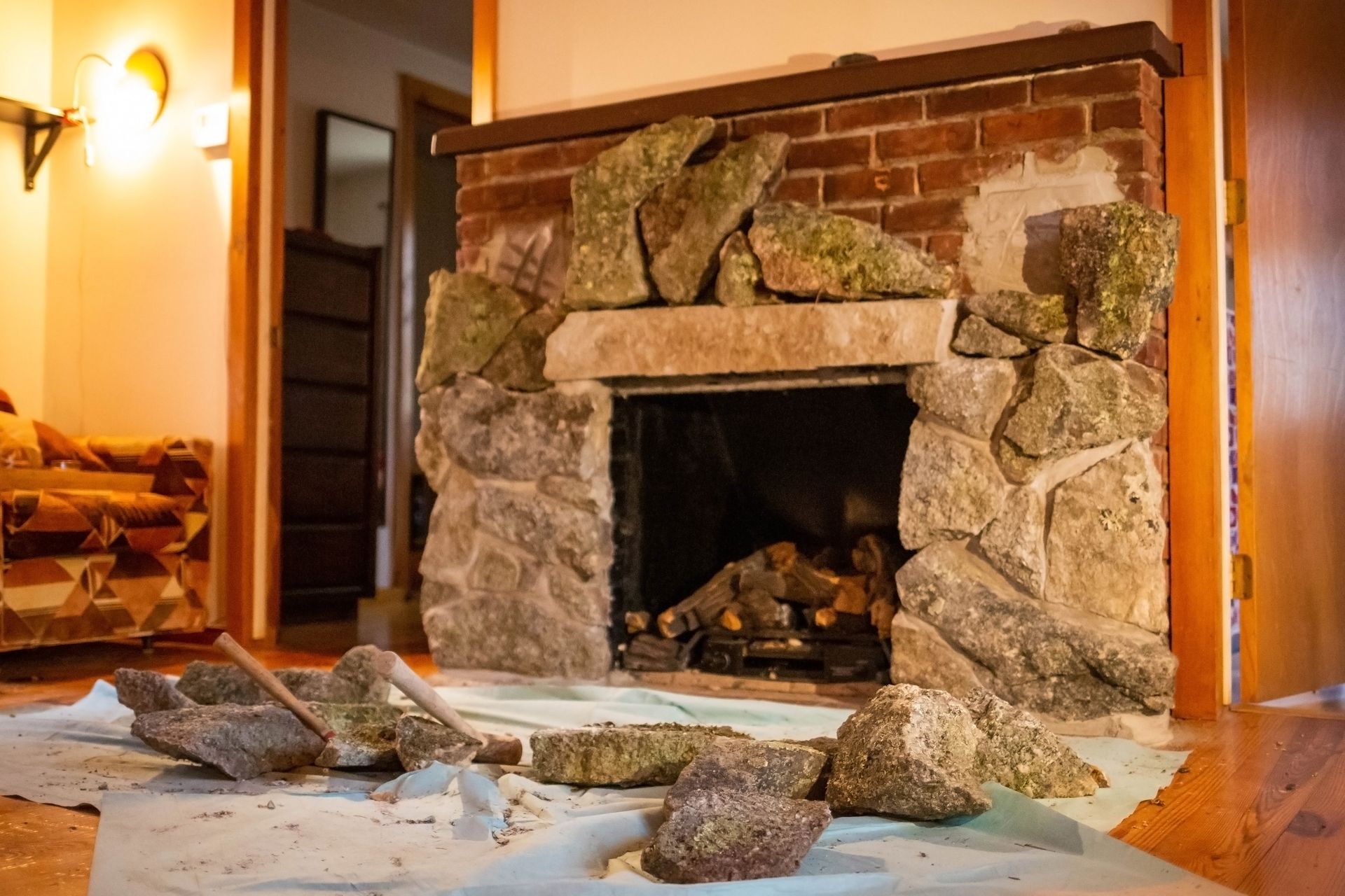 Fireplace being renovated with stone and exposed brick, debris on floor.