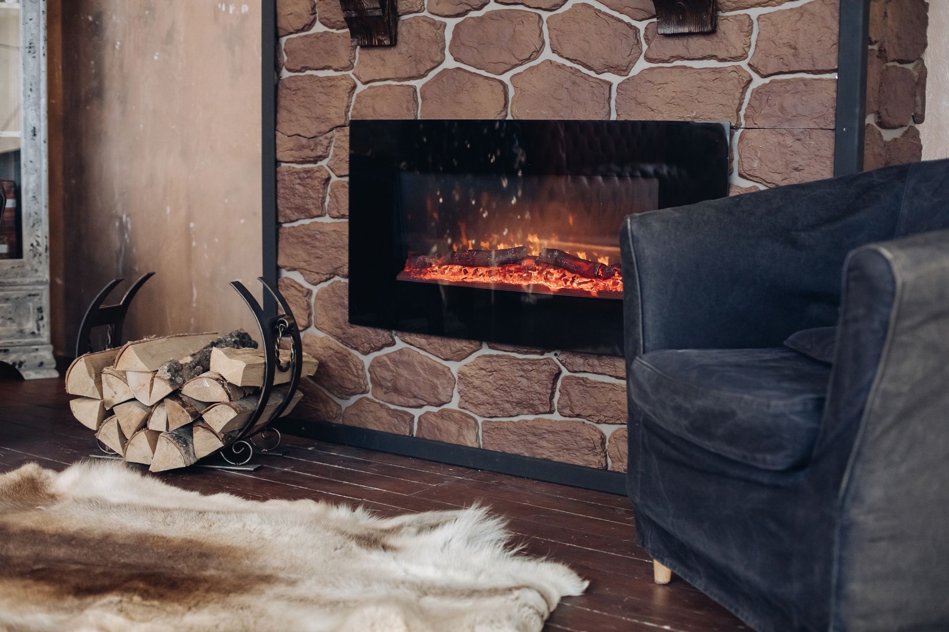 Fireplace with a glowing fire, stone surround, and armchair in a cozy interior.