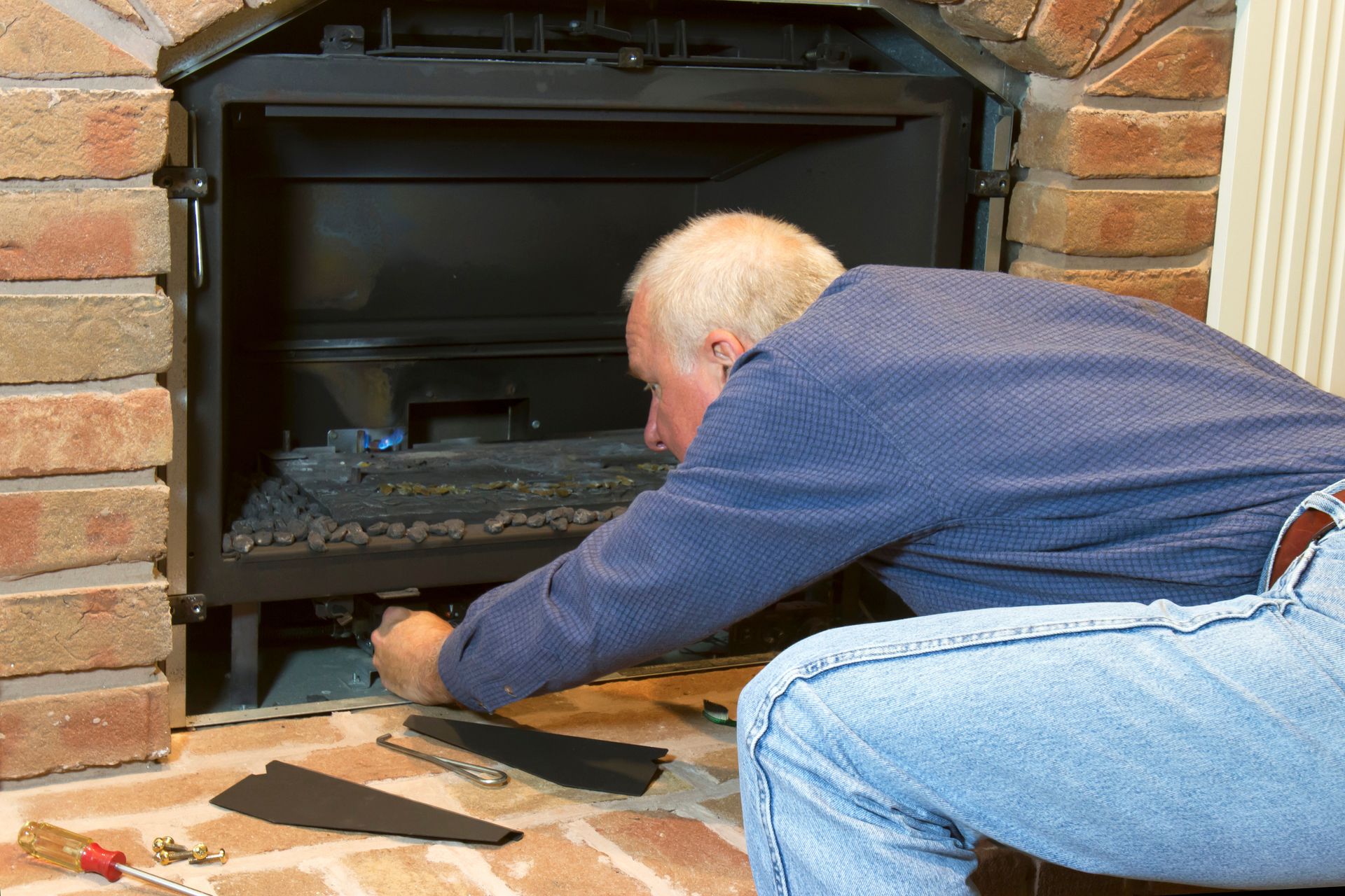 Man kneeling, working on fireplace, brick surround.