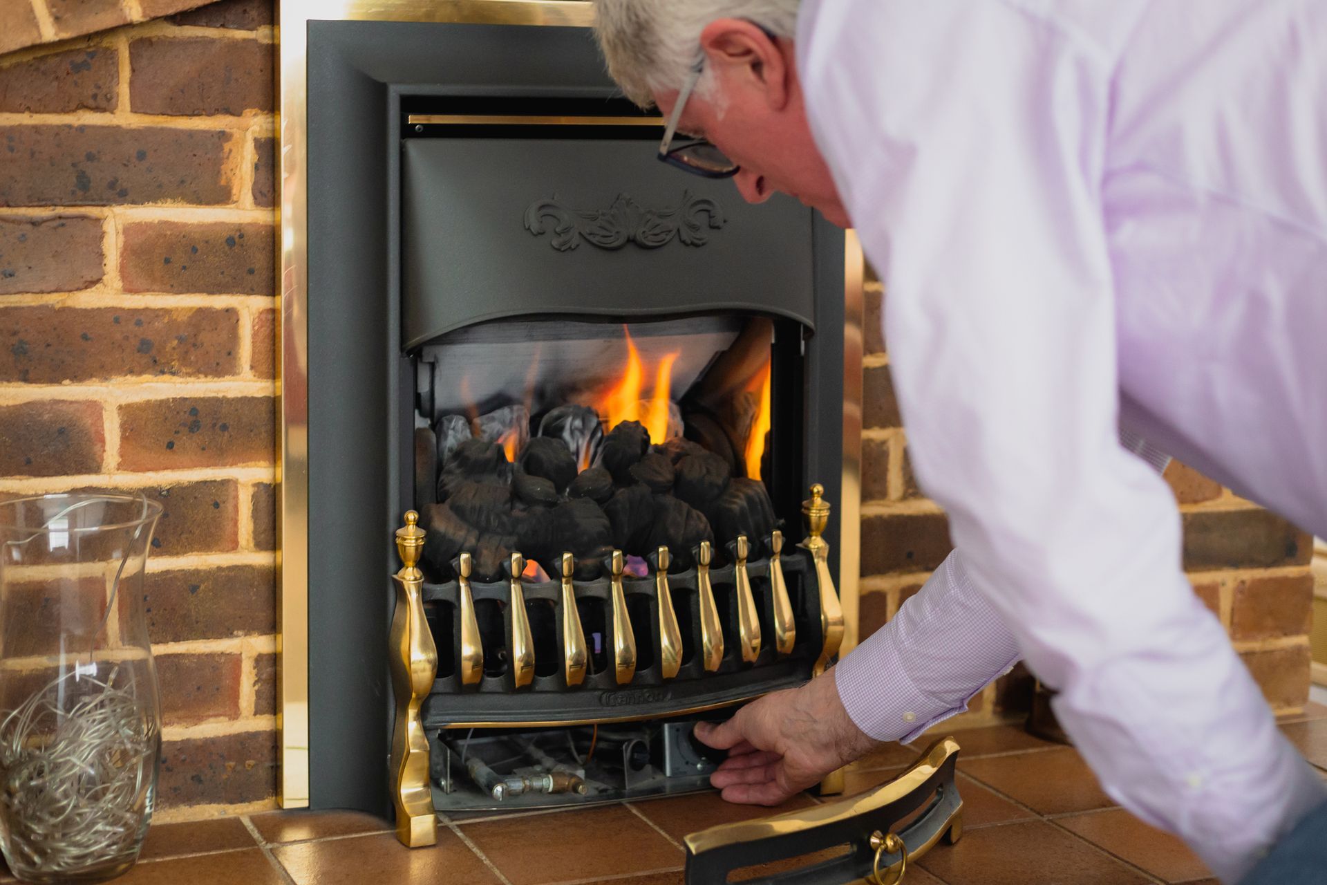 Man inspecting a lit fireplace with gold accents and brick surround.