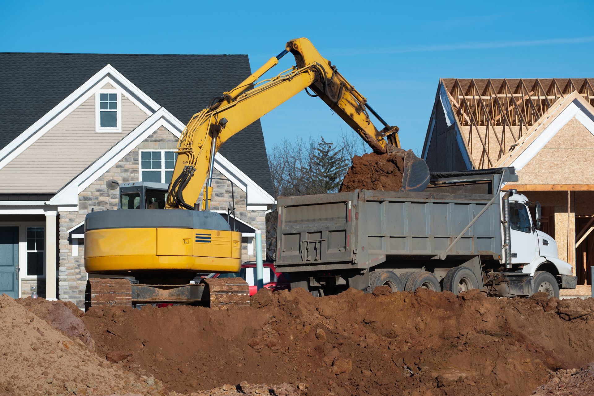 Yellow excavator loading dirt into a dump truck at a residential construction site.