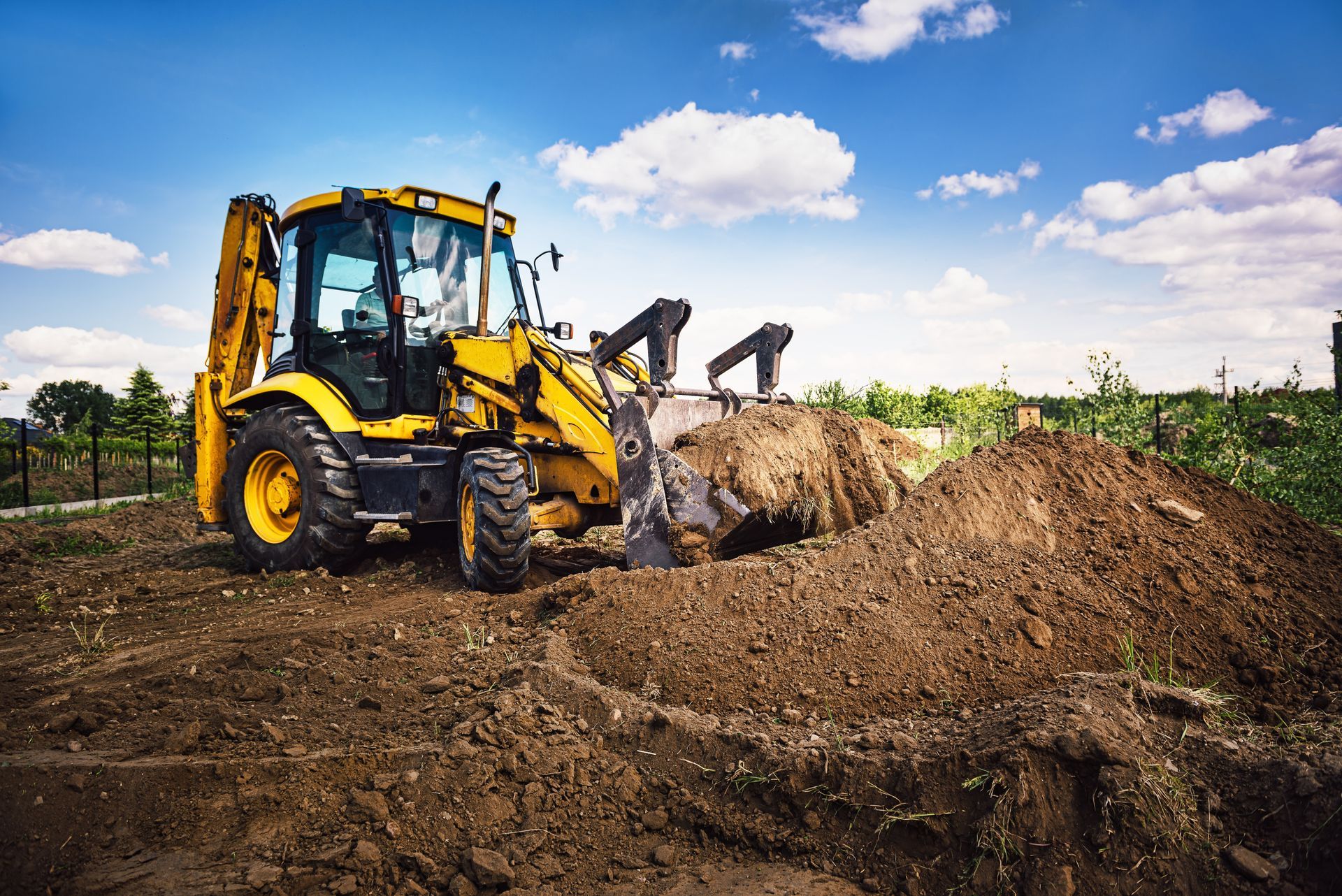 Yellow backhoe digging in dirt under a blue sky.