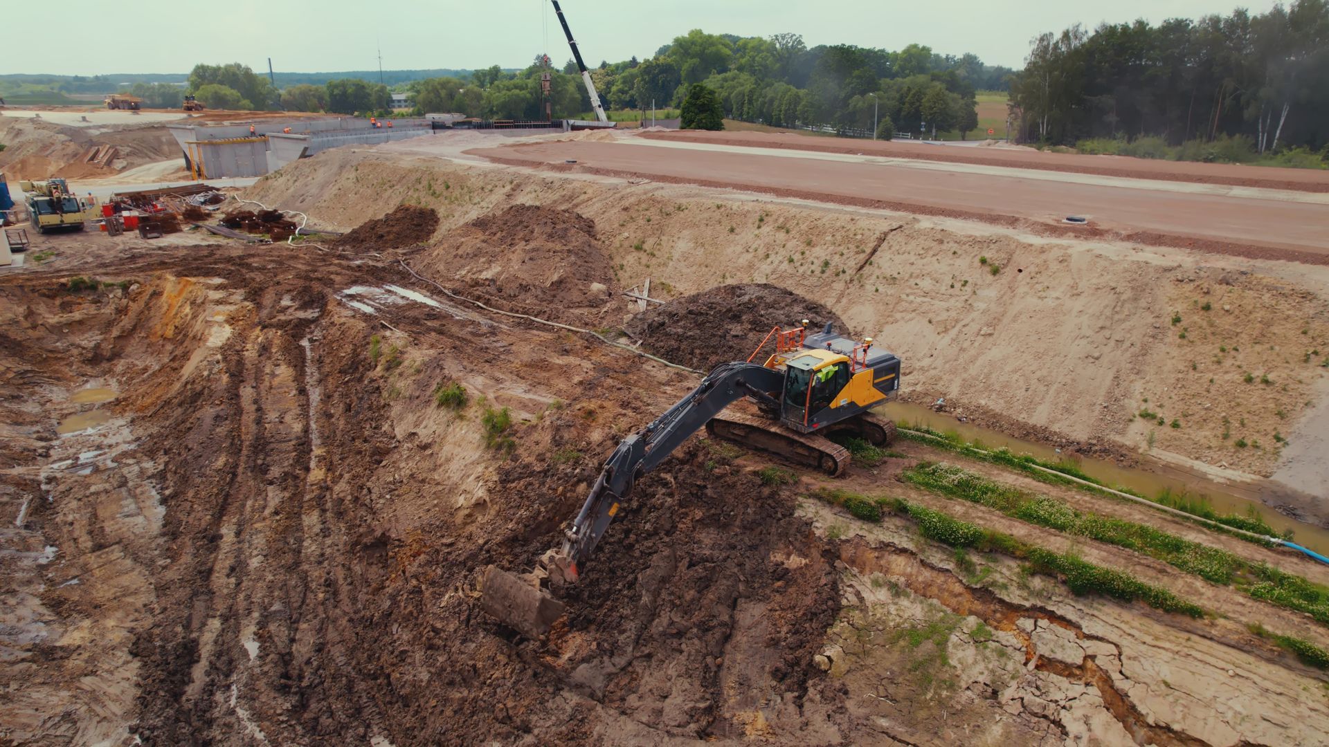 An excavator digs into a large dirt mound on a construction site.