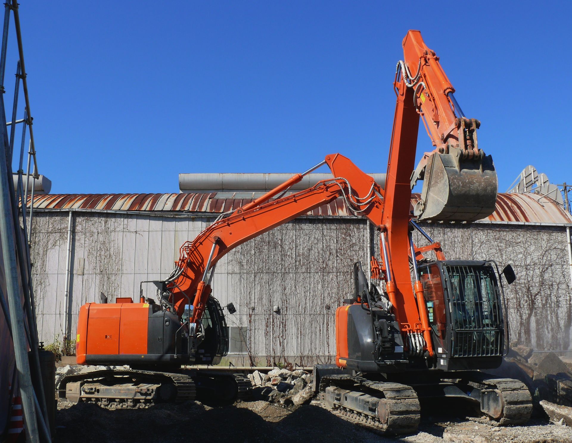 Two orange excavators on a construction site; one with bucket raised.