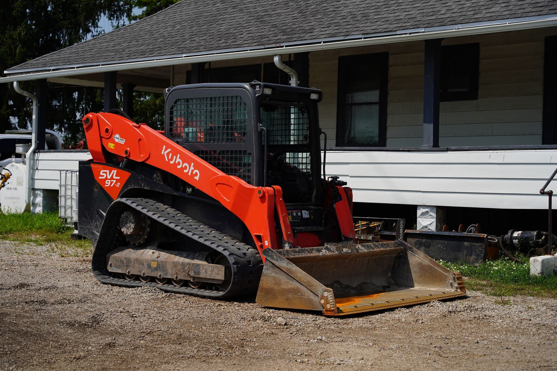Orange Kubota track loader parked on gravel in front of a white house.