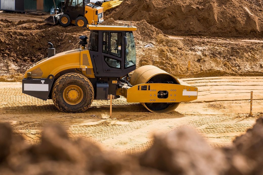 Yellow road roller compacting soil at a construction site.