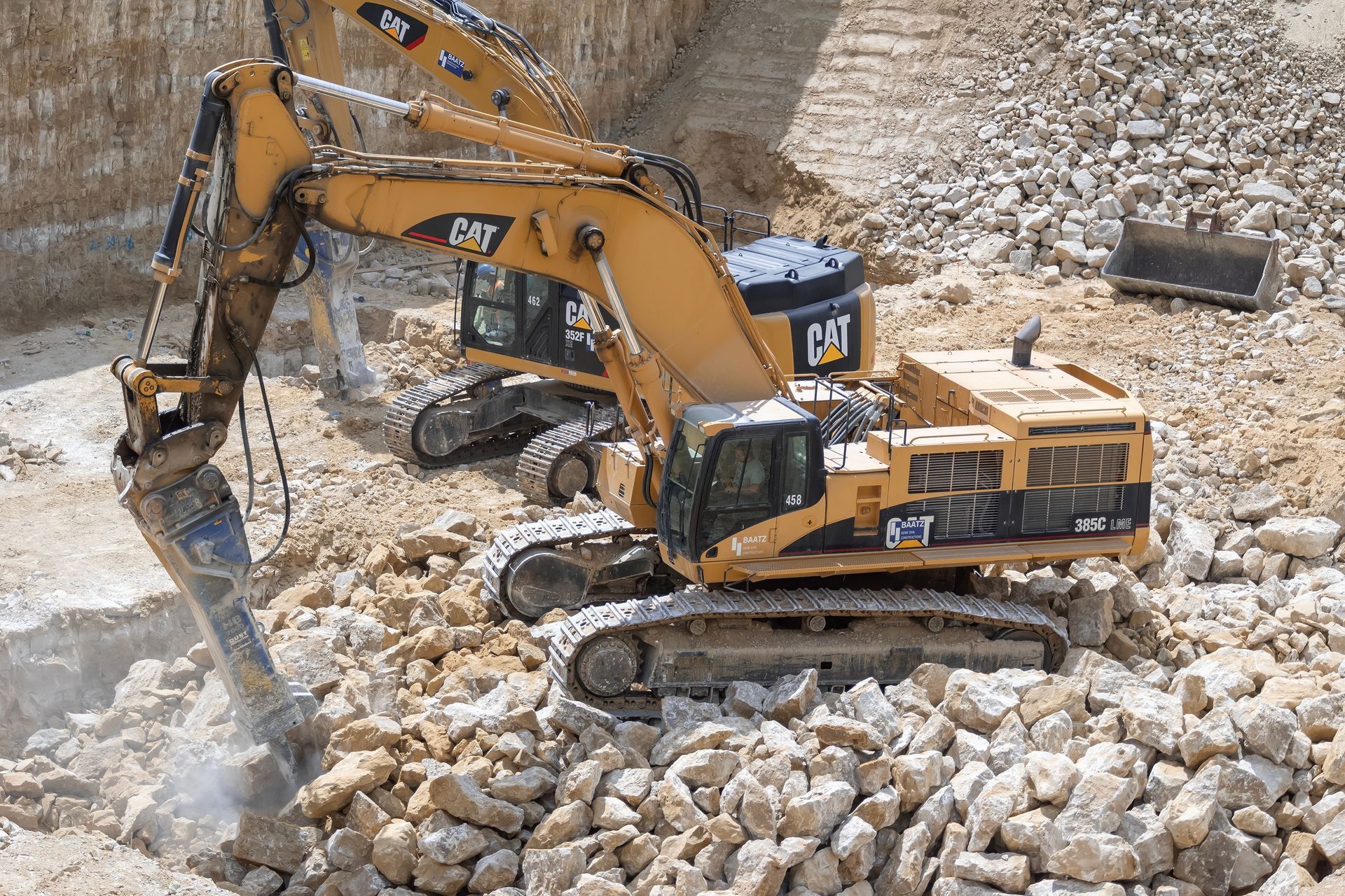 Two yellow Caterpillar excavators breaking rocks in a construction site.