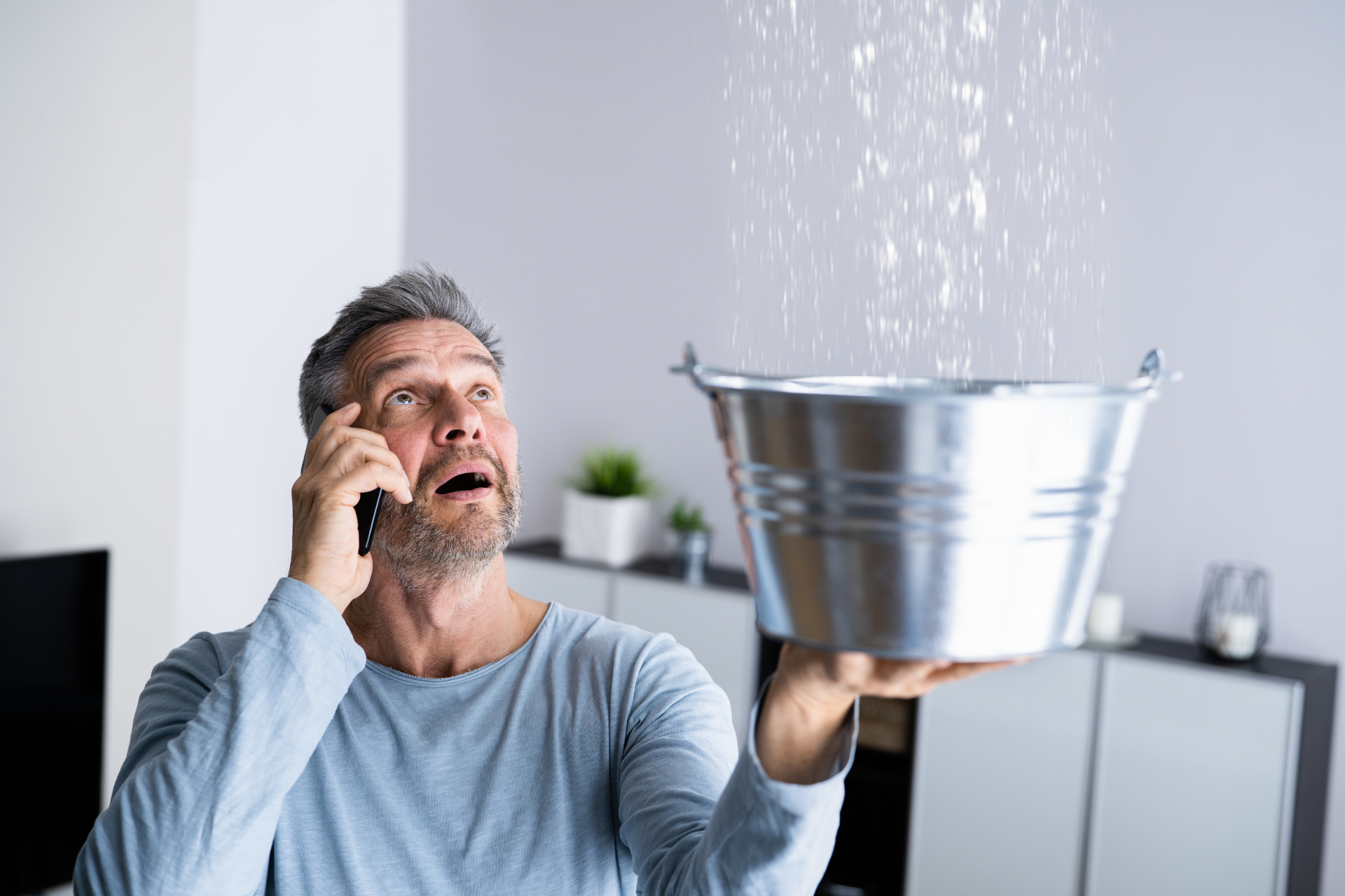 A man is talking on a cell phone while holding a bucket of water.