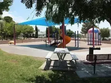 Henderson Artificial Turf - enhances recreational spaces like this image of Bicentennial Park, which features a shaded playground with colorful equipment, picnic tables, benches, and surrounding greenery under large trees.