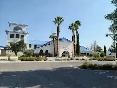 Henderson Artificial Turf -Modern white building with blue roof and Mediterranean architectural style, surrounded by tall palm trees and desert landscaping.