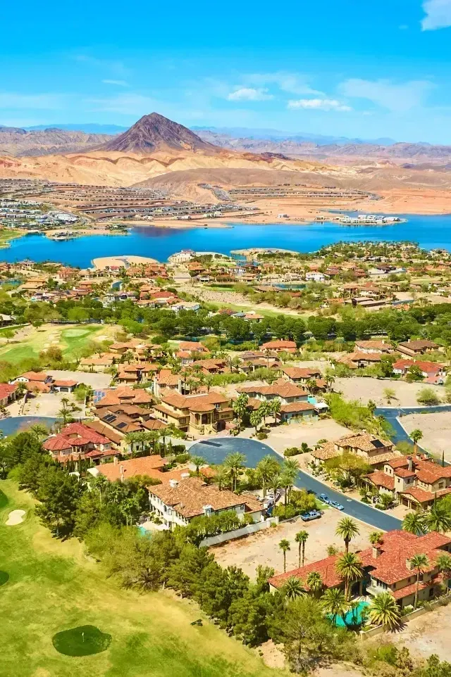 Henderson Artificial Turf - Aerial view of a picturesque community with terracotta-roofed homes near a lake, surrounded by desert mountains under a clear blue sky.