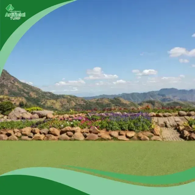 Henderson Artificial Turf - Vibrant flowers bloom in a tiered garden with a stone wall, backed by green mountains under a blue sky with scattered clouds.