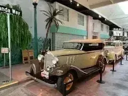 Henderson Artificial Turf - A vintage 1930s car on display in a museum, with palm trees and retro décor in the background. Street sign reads 