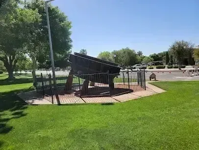 Henderson Artificial Turf - A large, rusted frying pan is displayed outdoors on a brick platform surrounded by a metal fence, set against a park with lush green grass and trees.